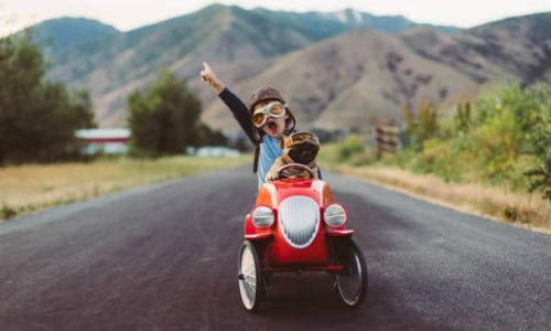 A young boy with flying goggles and flight cap races a red toy car with his pet and best friend French Bulldog along a small road in Utah, USA. Sometimes a road trip journey with your best friend and some fresh air in your face is the best medicine for the soul.